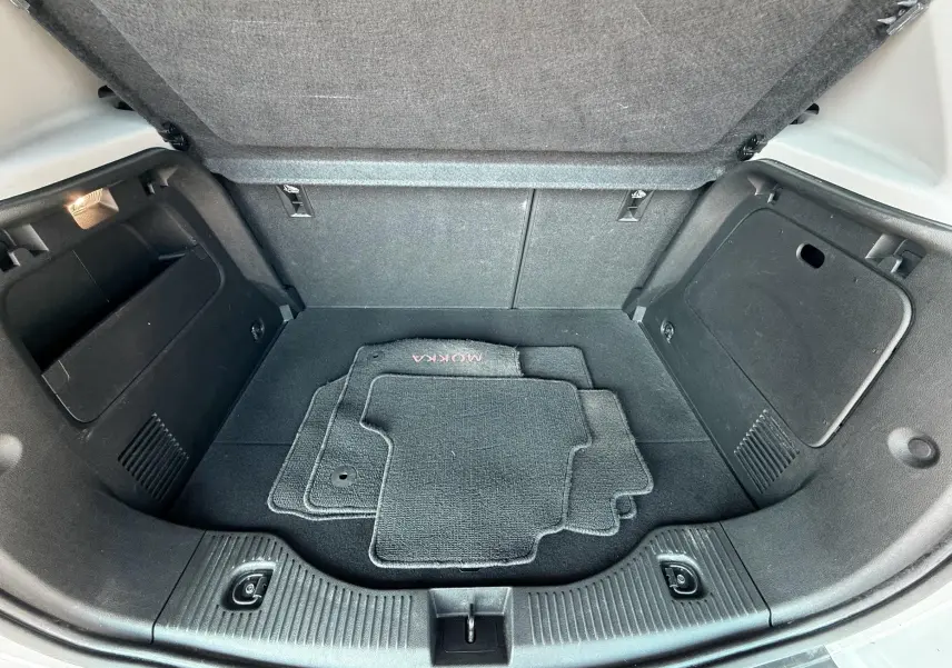 Vue ouverte du coffre arrière noir de l'Opel Mokka X blanc avec tapis de sol gris marqués MOKKA.