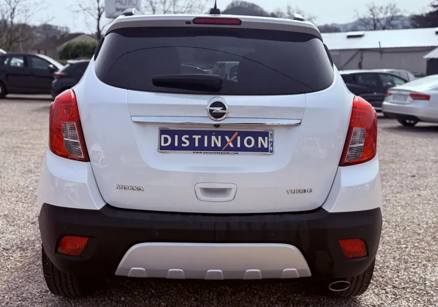 Vue arrière d’un Opel Mokka X blanc avec plaques Distinxion, feux rouges et pare-chocs noir contrastant.