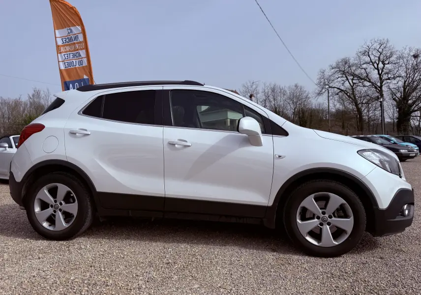 Vue de profil côté gauche d'un Opel Mokka X blanc avec jantes alliage et toit noir sur un parking extérieur.