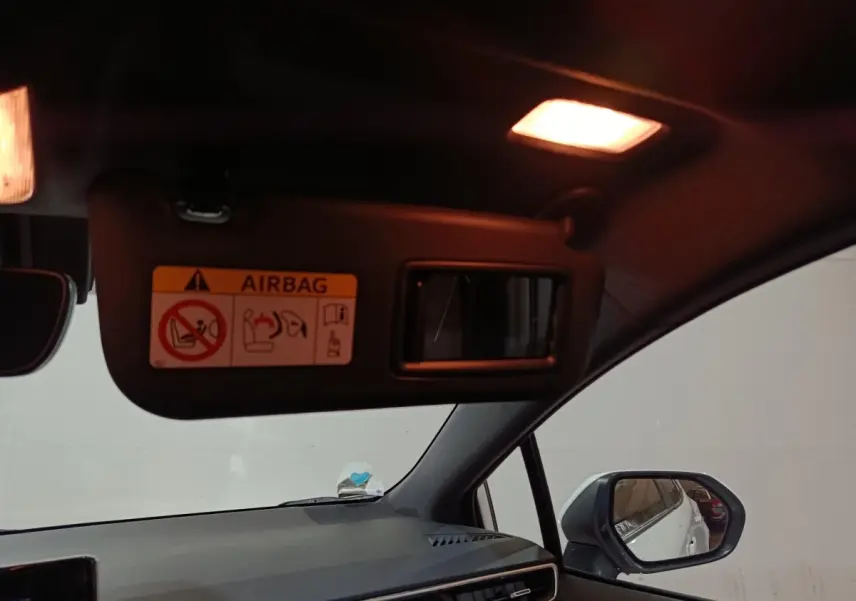 Vue intérieure côté conducteur de la Toyota Corolla hybride blanche, avec pare-soleil et rétroviseur extérieur visibles.