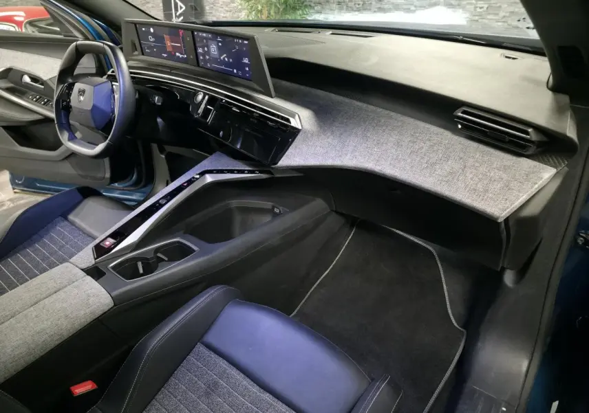 Vue intérieure côté passager du Peugeot 5008 bleu 2025, avec tableau de bord et console centrale au décor tissu gris et noir laqué.