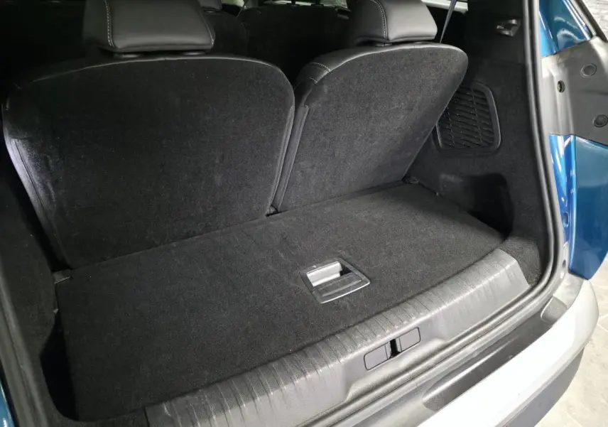 Coffre ouvert vu de l'arrière d'un Peugeot 5008 bleu 2025, banquette arrière partiellement rabattue et intérieur noir.