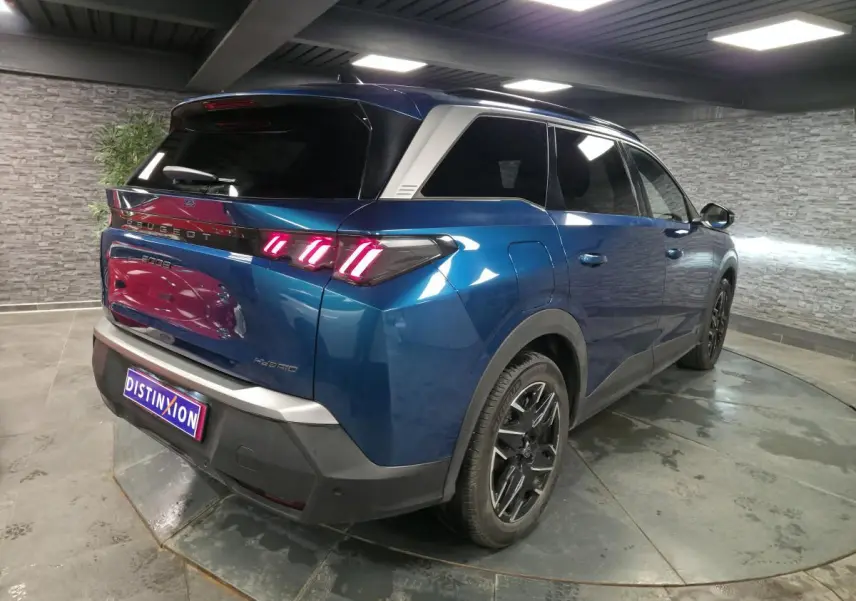 Peugeot 5008 hybride bleu métallisé vue 3/4 arrière droit avec feux arrière LED à 3 griffes et jantes alliage noires.