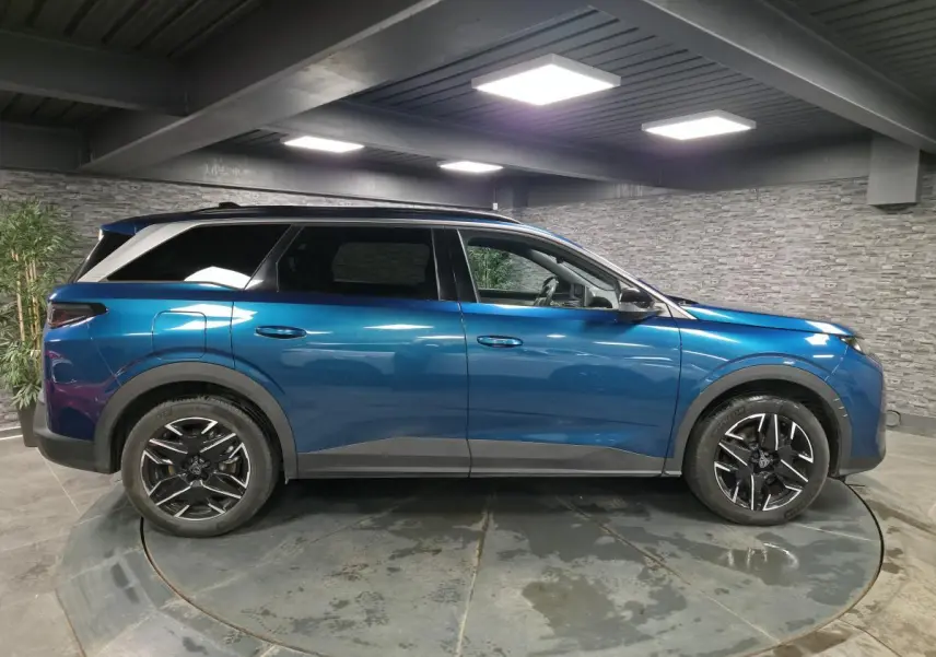 Vue de profil côté gauche d'un Peugeot 5008 bleu métallisé 2025 avec jantes alliage noires et barres de toit.