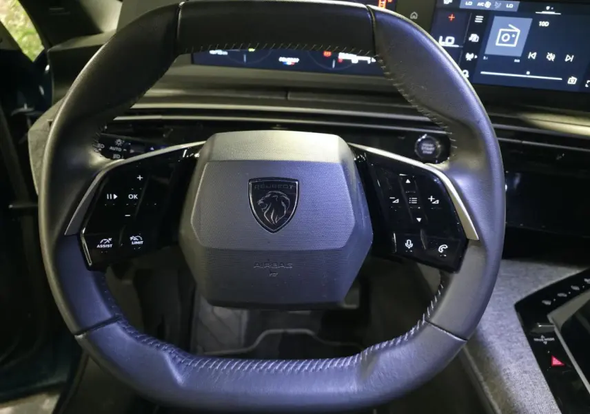 Volant cuir noir de la Peugeot 5008 2025 avec commandes intégrées et tableau de bord numérique en arrière-plan.