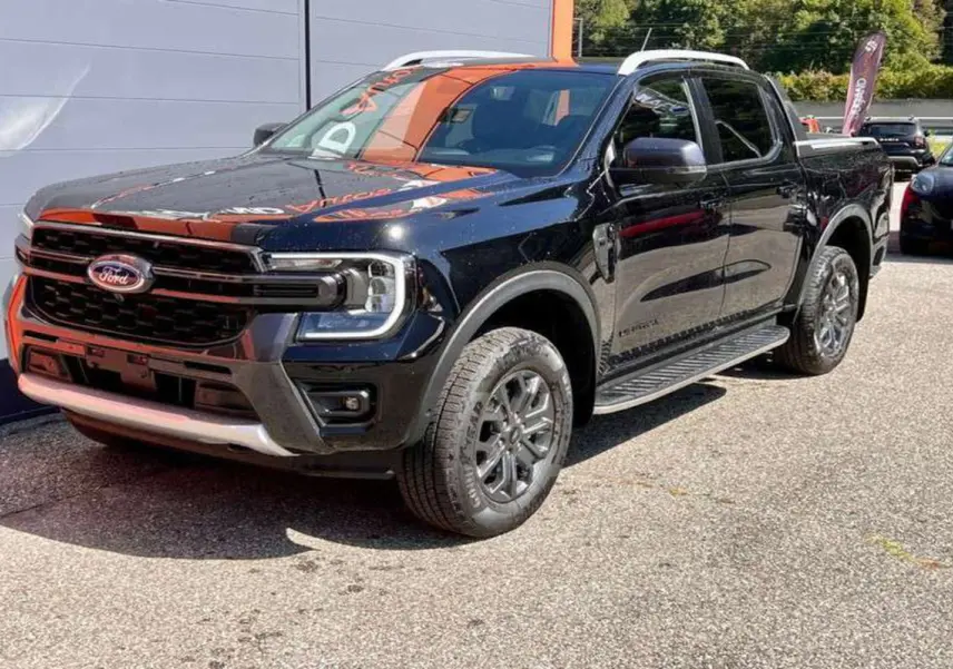 Ford Ranger 3.0 V6 Wildtrak Plus noir agate en 3/4 avant droit, avec jantes alu et marchepieds visibles.