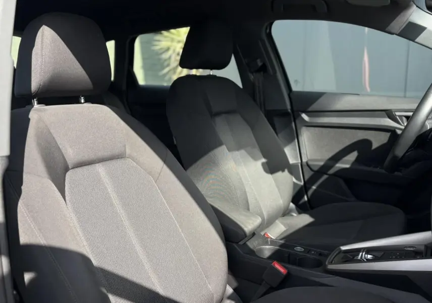 Vue intérieure sur les sièges avant en tissu gris de l'Audi A3 Sportback 30 TFSI 2023 avec accoudoir central réglable.