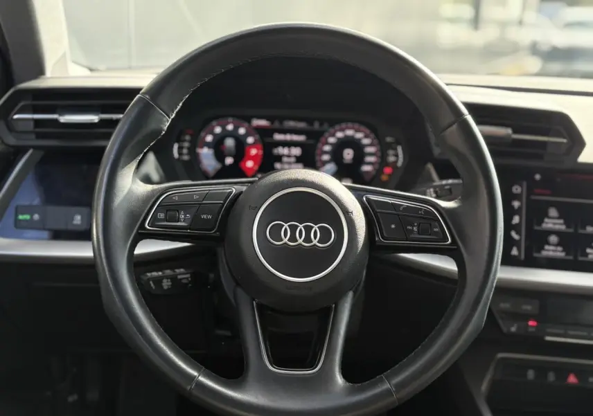 Vue rapprochée du volant en cuir noir de l'Audi A3 Sportback 2023 avec tableau de bord numérique et commandes intégrées.