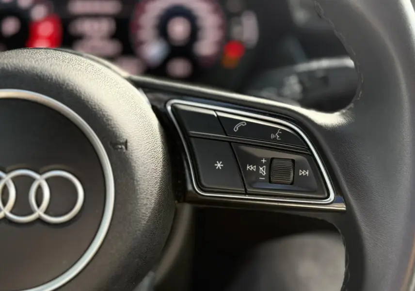 Gros plan sur les commandes du volant d'une Audi A3 Sportback 30 TFSI 2023, finition Design en Noir Mythe.