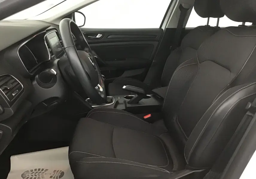 Intérieur côté conducteur de la Renault Mégane IV Berline blanche, montrant sièges noirs et tableau de bord avec volant multifonction.
