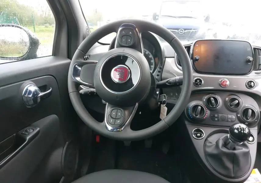Vue intérieure centrée sur le volant et la console d'une Fiat 500 2023, avec boîte manuelle et tableau de bord gris Electroclash.
