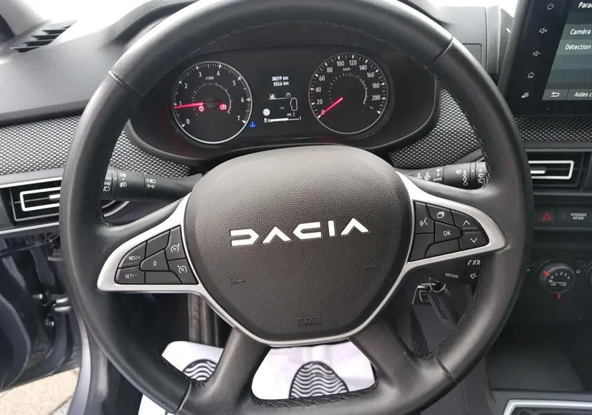 Vue rapprochée du volant noir de la Dacia Sandero 2024 avec commandes intégrées et tableau de bord visible.