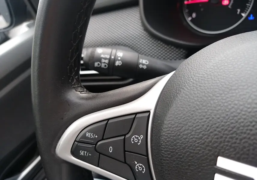 Gros plan sur les commandes de régulateur de vitesse au volant noir d’une Dacia Sandero 2024 gris, intérieur conducteur.