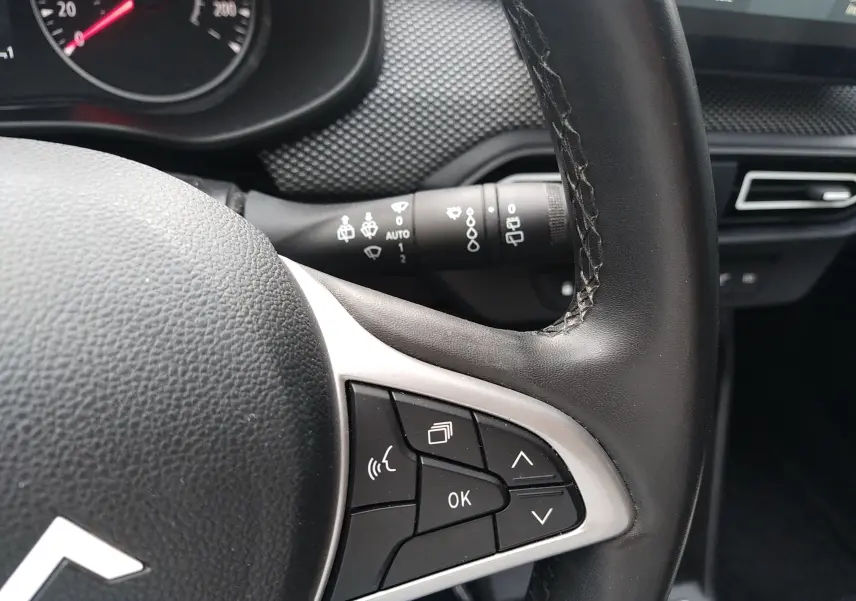 Gros plan sur le volant côté gauche de la Dacia Sandero 2024 gris, avec commandes multifonctions et commodo d’essuie-glace visible.