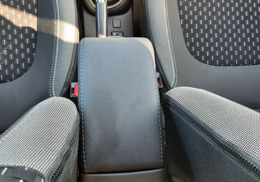 Vue plongeante sur l'accoudoir central noir et les sièges en tissu gris du Renault Captur 2018 essence.