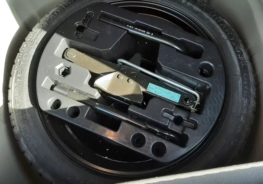 Gros plan sur la roue de secours noire et son kit d'outils intégré dans le coffre d'un Renault Captur gris cassiope toit noir.