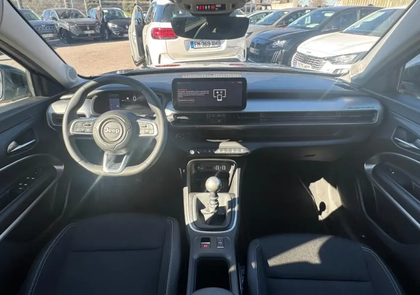 Vue intérieure avant du Jeep Avenger gris 2025, avec tableau de bord moderne et levier de vitesse manuel.