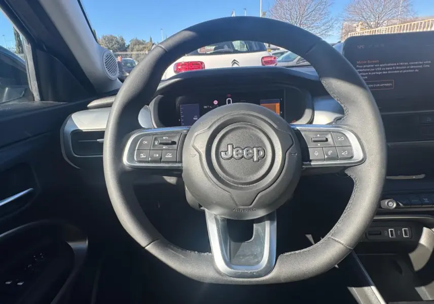 Vue intérieure centrée sur le volant noir du Jeep Avenger 2025, avec tableau de bord et écran digital en arrière-plan.