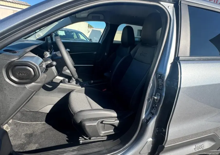 Vue intérieure côté conducteur du Jeep Avenger gris 2025, avec sièges en tissu et logo Jeep brodé sur l'appui-tête.