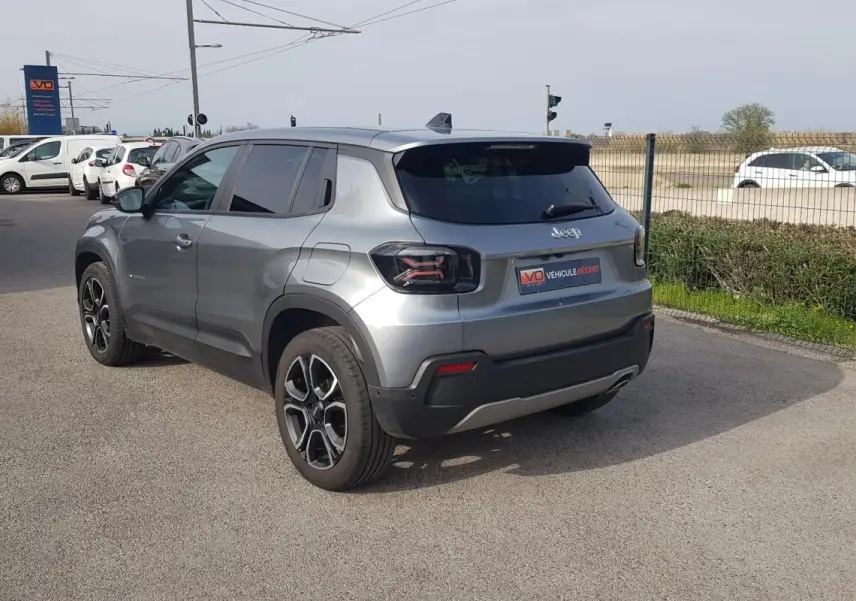 Vue 3/4 arrière gauche d’un Jeep Avenger gris métallisé avec jantes alliage 18 pouces, garé en extérieur.