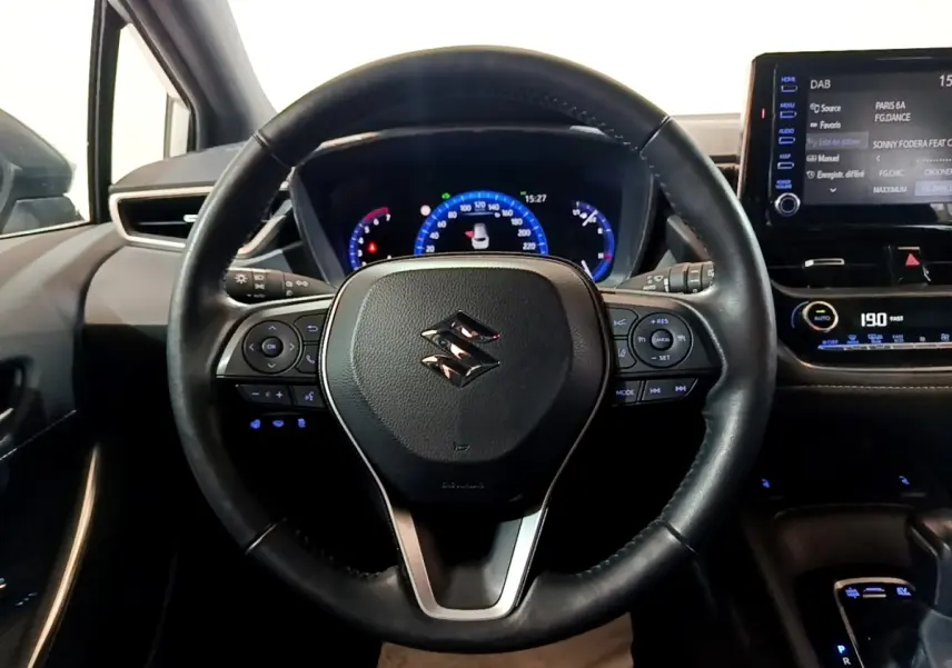 Vue rapprochée du volant cuir et alu multifonctions de la Suzuki Swace 1.8 Hybrid Privilege avec tableau de bord digital.