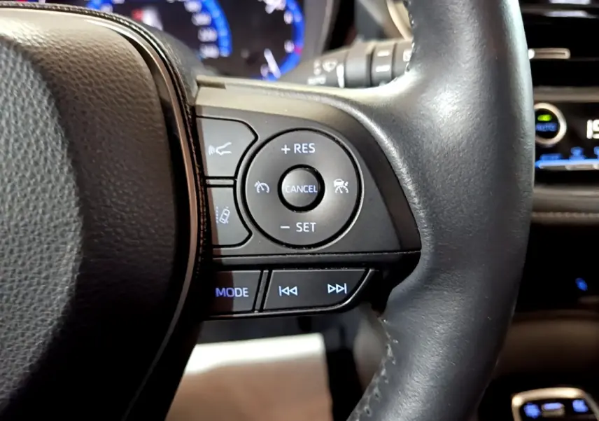 Gros plan sur le volant cuir et alu multifonctions noir du Suzuki Swace gris clair, avec commandes de régulateur et audio.