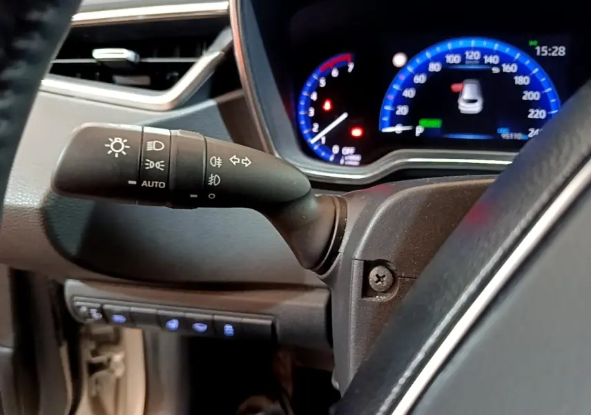 Gros plan sur la manette de commande des phares et clignotants à gauche du volant dans l’habitacle du Suzuki Swace gris clair.