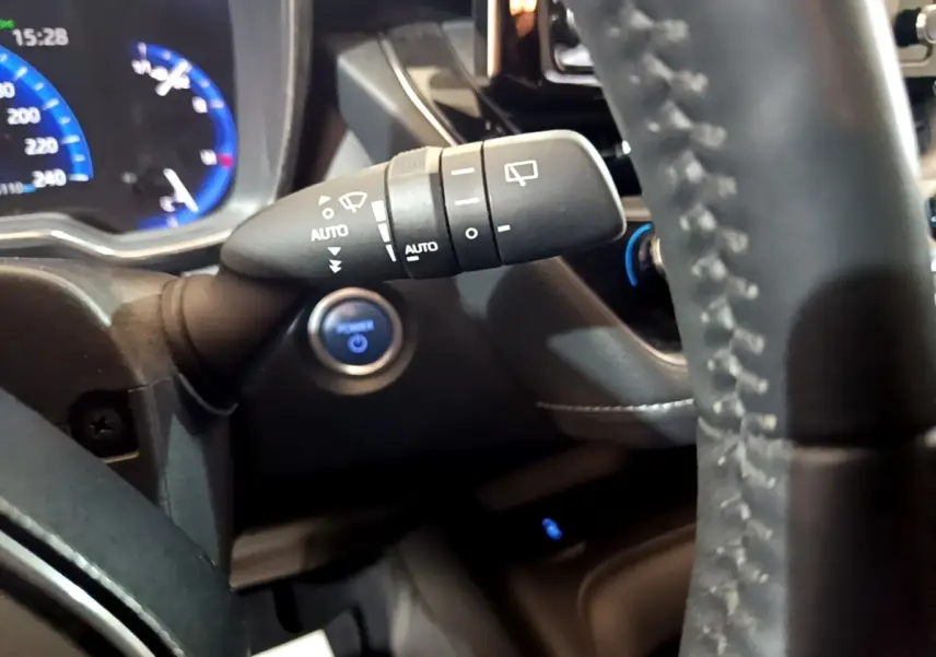 Gros plan intérieur sur la manette d’essuie-glace et le volant cuir du Suzuki Swace gris clair, avec tableau de bord digital bleu.