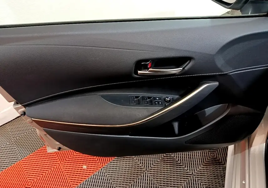 Vue intérieure côté gauche de la porte avant grise claire du Suzuki Swace 1.8 Hybrid Privilege avec poignée alu et commandes vitres.