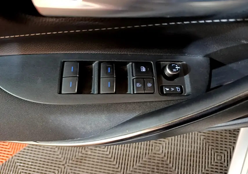 Vue rapprochée des commandes de lève-vitres et réglage des rétroviseurs sur la porte côté conducteur d'une Suzuki Swace gris clair.