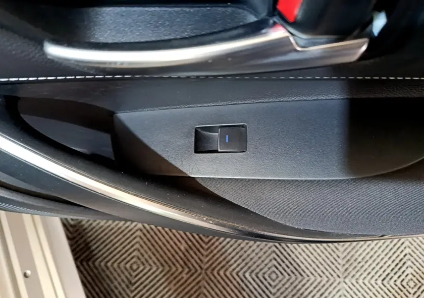 Détail de l'intérieur côté porte avant avec bouton de verrouillage, garniture noire et surpiqûres blanches.