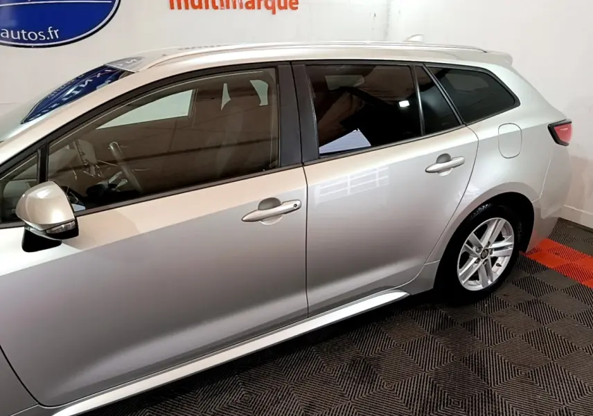 Profil côté gauche de la Suzuki Swace gris clair 2021 avec vitres teintées et jantes alliage visibles en intérieur showroom.