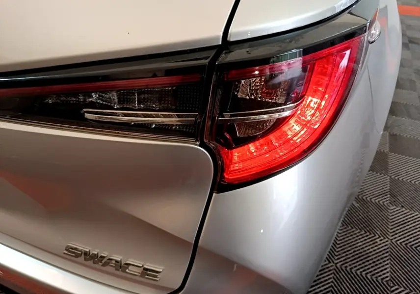 Gros plan sur le feu arrière droit d'une Suzuki Swace gris clair, mettant en valeur le logo et la finition lisse du coffre.