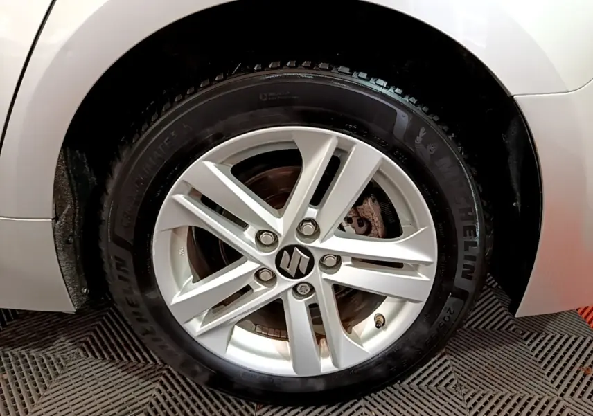 Gros plan sur la roue avant gauche gris clair d'une Suzuki Swace 1.8 Hybrid Privilege avec jante alliage.