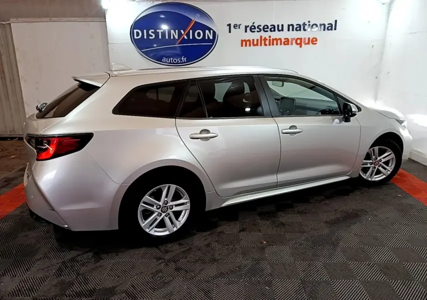 Vue de profil droit d'une Suzuki Swace 1.8 Hybrid Privilège gris clair en stationnement intérieur sur sol à motifs.