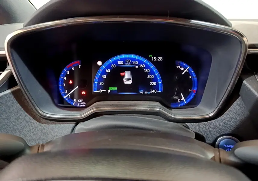 Vue rapprochée du tableau de bord numérique bleu de la Suzuki Swace 1.8 Hybrid Privilege avec volant partiellement visible.