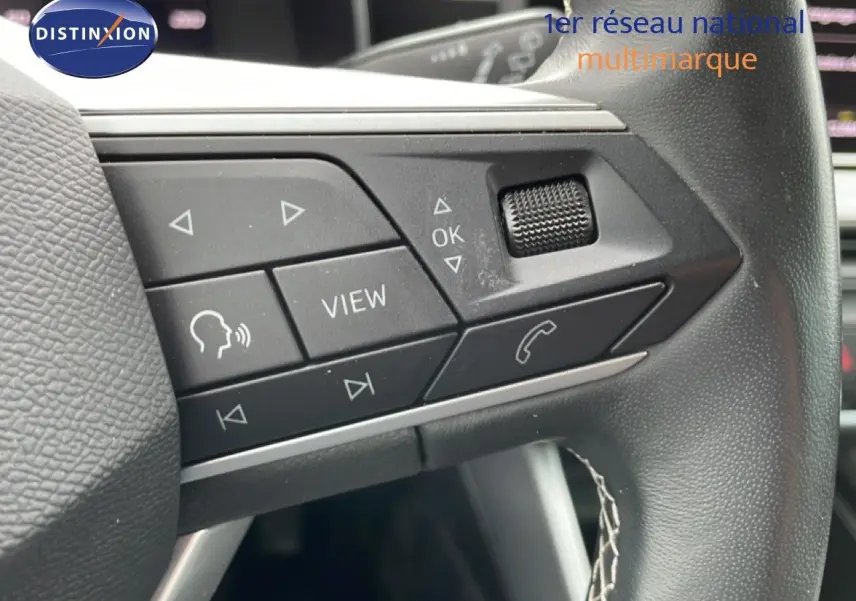 Gros plan sur les commandes au volant côté gauche du SEAT LEON ST bleu Fjord, version 2025 avec boutons multifonctions.