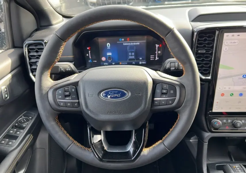 Vue intérieure centrée sur le volant cuir noir avec surpiqûres marron et tableau de bord numérique du Ford Ranger 2025.