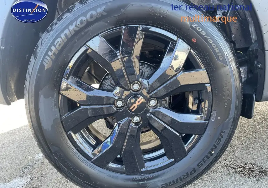 Gros plan sur la jante alu noire brillante d'une Dacia Sandero Stepway gris schiste avec pneu Hankook humide.