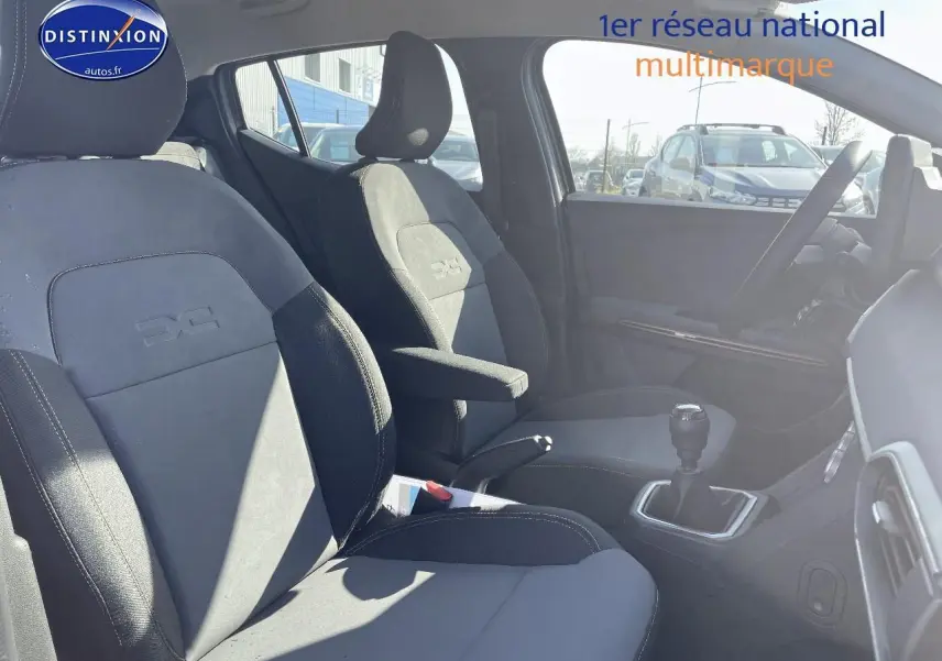 Intérieur avant de la Dacia Sandero Stepway 2025, sièges gris avec accoudoir central et levier de vitesse manuel visible.