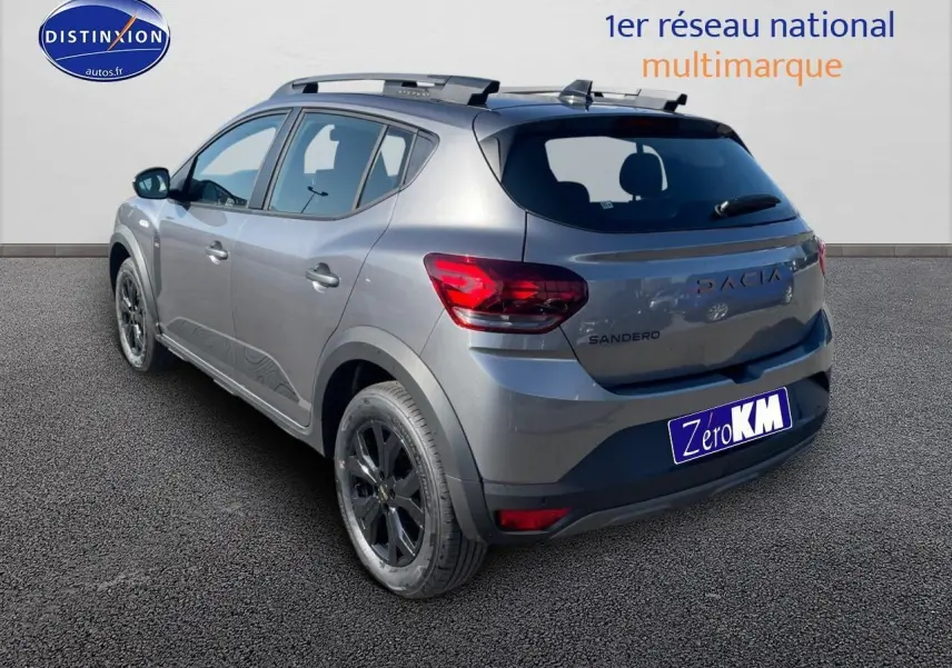 Vue 3/4 arrière droite d'une Dacia Sandero gris schiste avec barres de toit et jantes alu noires.