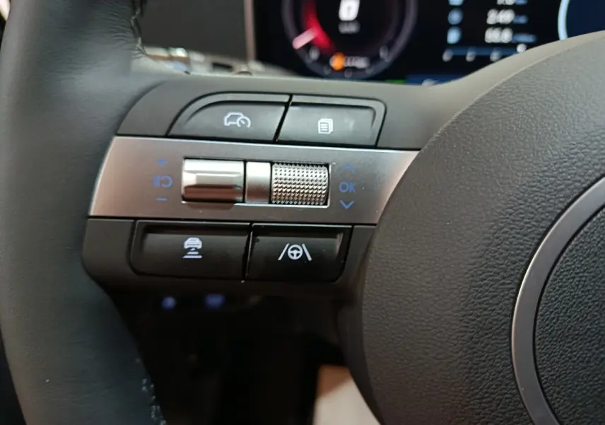 Gros plan sur les commandes de régulateur de vitesse et assistance au volant à gauche du volant du Hyundai Tucson gris clair 2025.