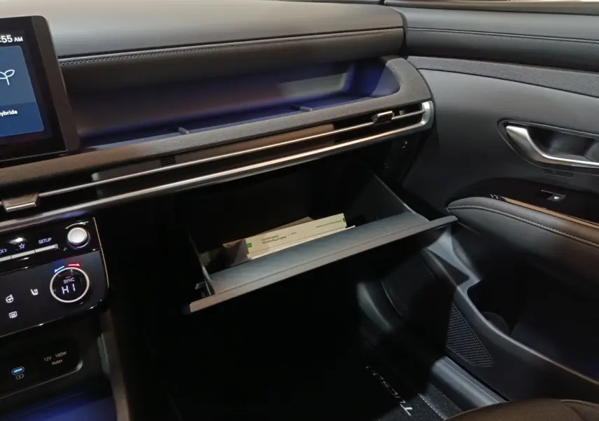 Intérieur côté passager du Hyundai Tucson 2025, tableau de bord noir avec boîte à gants ouverte et écran tactile visible.