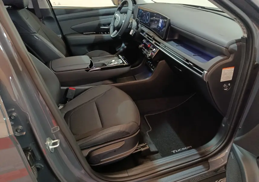 Intérieur avant droit du Hyundai Tucson gris clair 2025, avec tableau de bord numérique et sièges noirs.