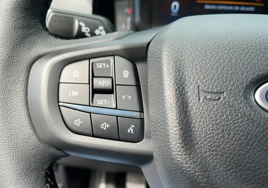 Gros plan sur les commandes de régulateur et volume au volant cuir noir du Ford Ranger gris carbone 2025.