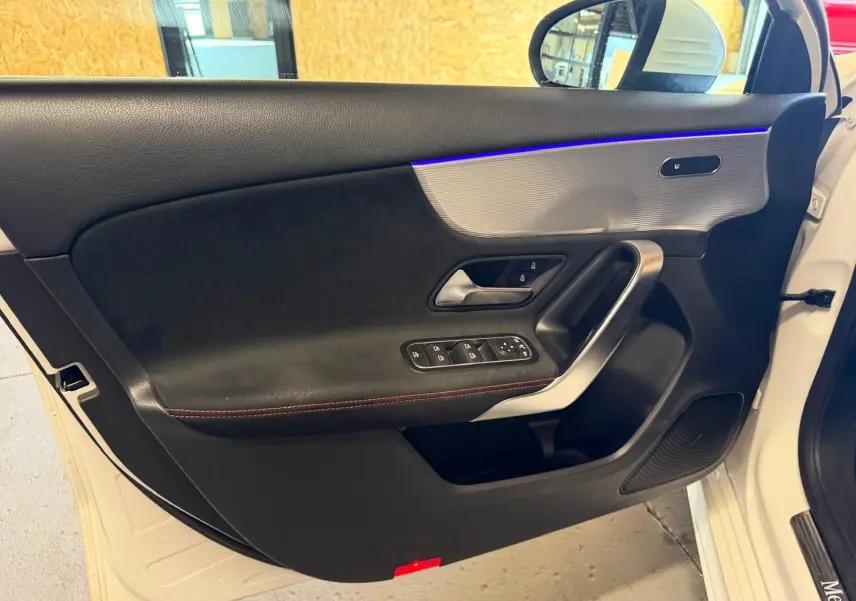 Vue intérieure côté gauche de la porte avant blanche d'une Mercedes Classe A 220D AMG Line avec éclairage d'ambiance bleu.