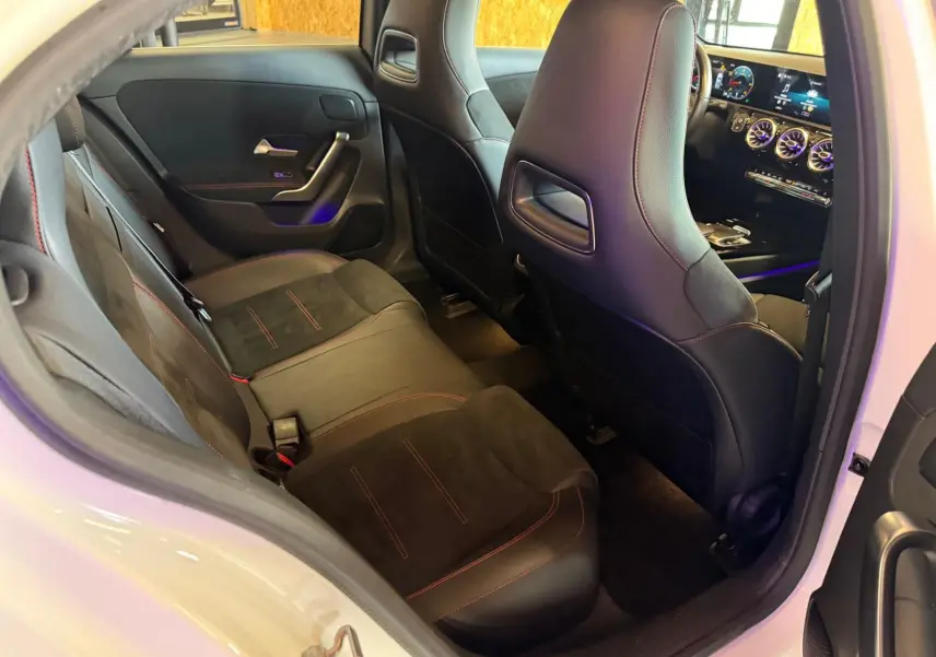 Vue intérieure depuis la porte arrière droite d'une Mercedes Classe A 220D AMG Line blanche, sièges noirs avec surpiqûres rouges.