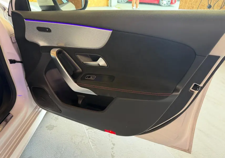 Vue intérieure côté gauche de la porte avant blanche d'une Mercedes Classe A 220D AMG Line avec éclairage d'ambiance violet.