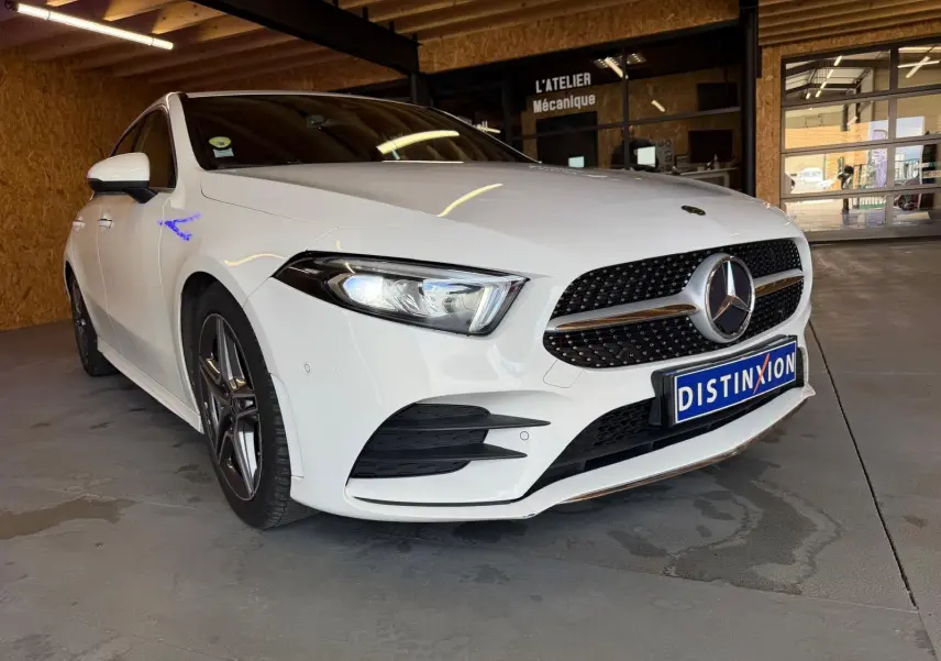 Mercedes Classe A 220D AMG Line blanche vue en 3/4 avant droit dans un garage avec calandre sportive et phares allumés.