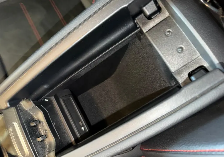 Vue rapprochée de la console centrale ouverte d’une Mercedes Classe A 220D AMG Line avec intérieur noir et surpiqûres rouges.